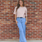 Woman wearing a beige top and blue jeans standing in front of a brick wall.
