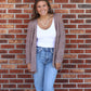 Woman wearing a cardigan, white top, and blue jeans standing against a brick wall.